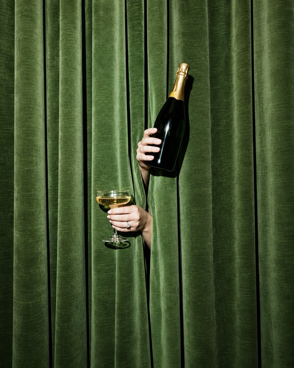 Una persona asomándose entre cortinas verdes con champagne
